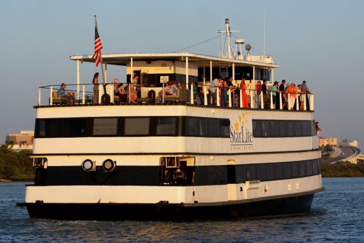 Large white boat with two decks, people onboard, American flag, on open water.