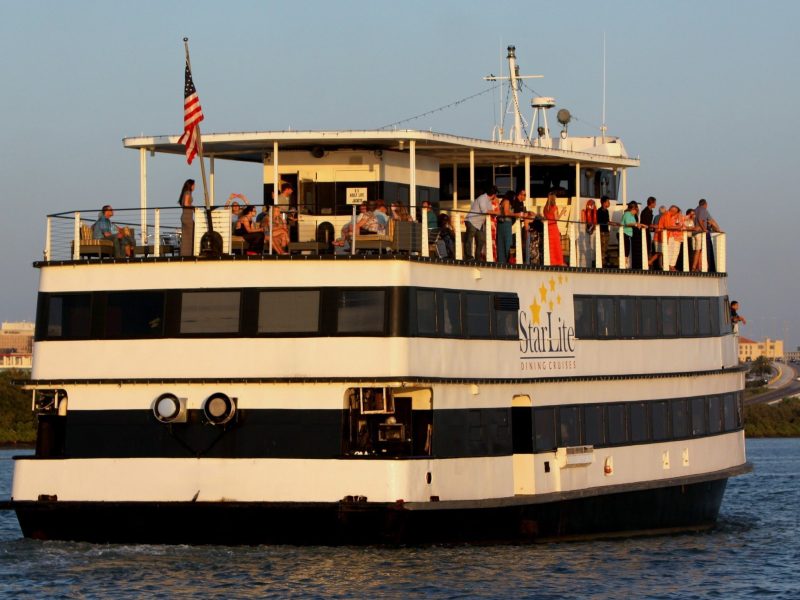 Large white boat with two decks, people onboard, American flag, on open water.