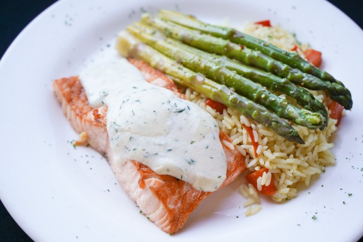 Salmon with dill sauce, asparagus, and rice on a white plate.