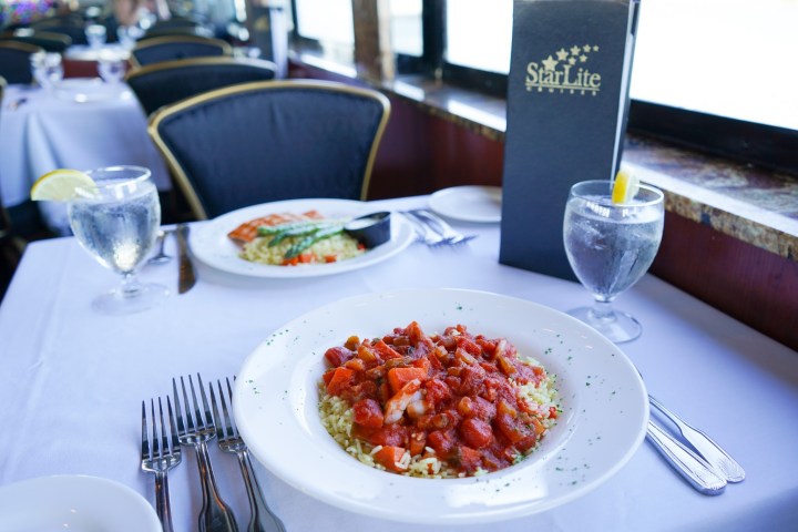 Two plates of food on a restaurant table with water glasses and a menu.