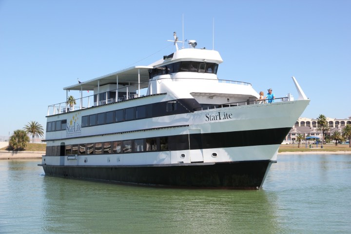 Large white and black cruise ship on calm water with clear blue sky.