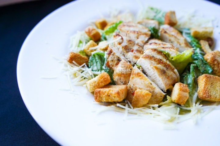 Grilled chicken Caesar salad with croutons on a white plate.