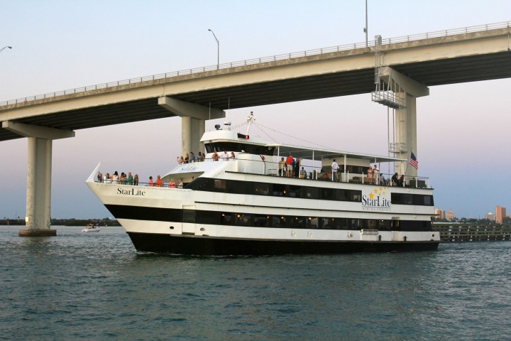 Large white and black cruise boat under a bridge on a calm waterway.