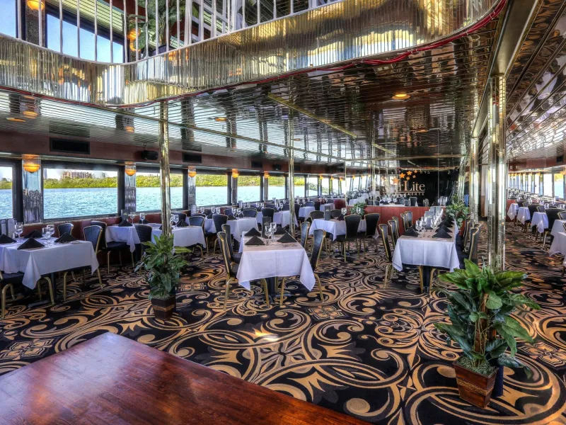 Elegant dining area on a boat with white tablecloths, patterned carpet, and lake view.