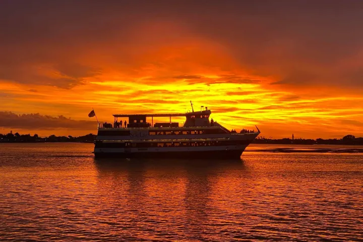 Ship silhouetted against a vibrant, orange sunset over calm waters.