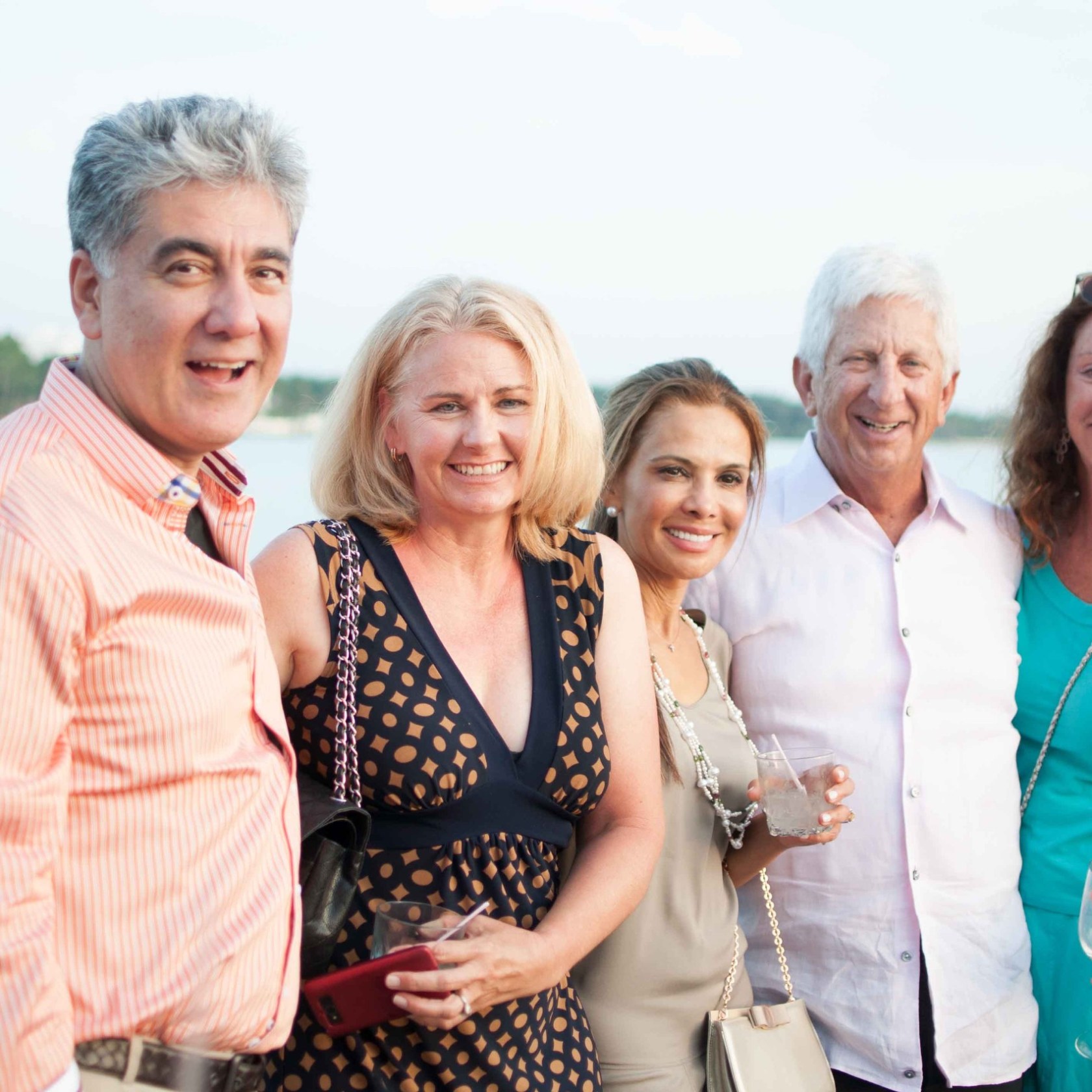 Group of five adults smiling on a boat deck by the water.