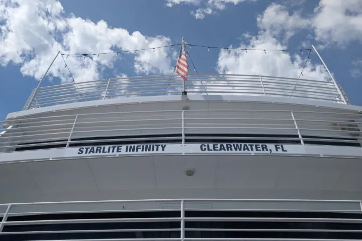Deck of a white ship named 'Starlite Infinity' with a U.S. flag and blue sky.
