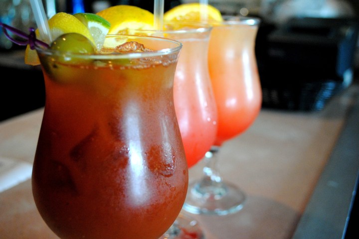 Three cocktails on a bar, garnished with fruit slices.