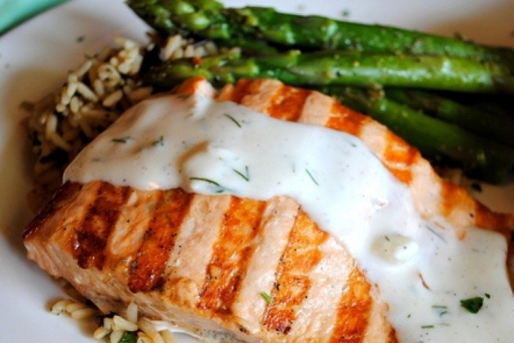 Grilled salmon with creamy sauce, asparagus, and rice on a plate.