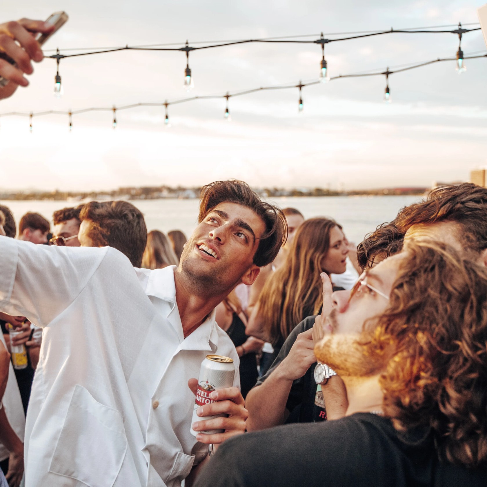 Group of friends taking a selfie at an outdoor party near water.