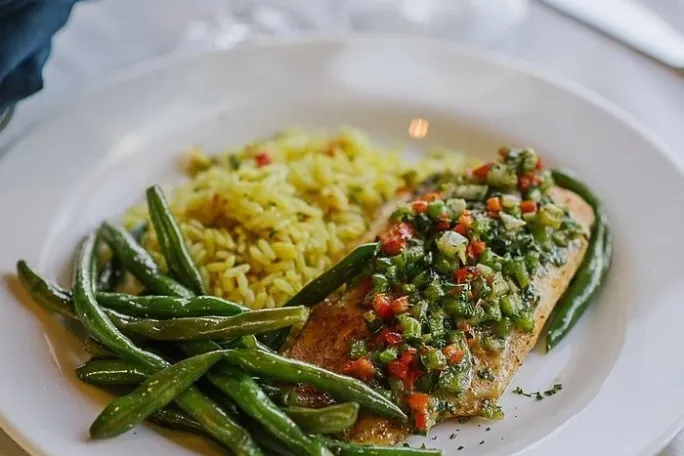 Fish with herbs, green beans, and rice on a white plate.