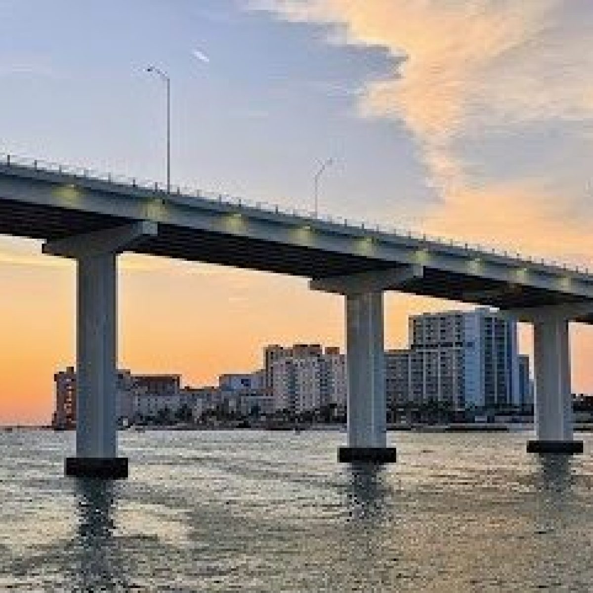 Bridge over water at sunset with buildings in the background.