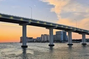 Bridge over water at sunset with buildings in the background.