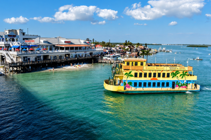 Yellow ferry near dock with buildings and people on beach.