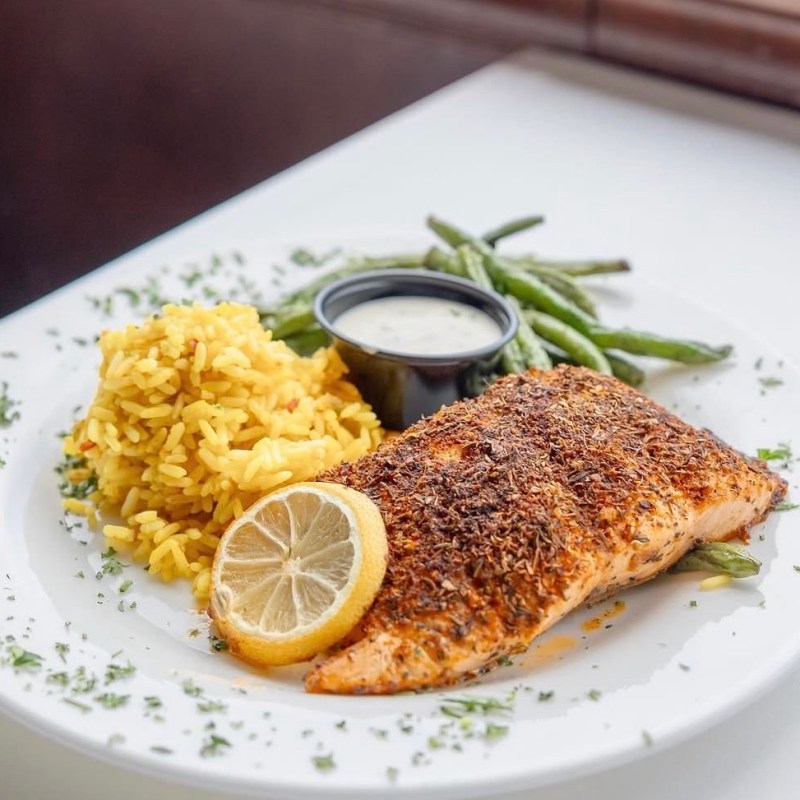 Grilled salmon with lemon, yellow rice, green beans, and sauce on a white plate.
