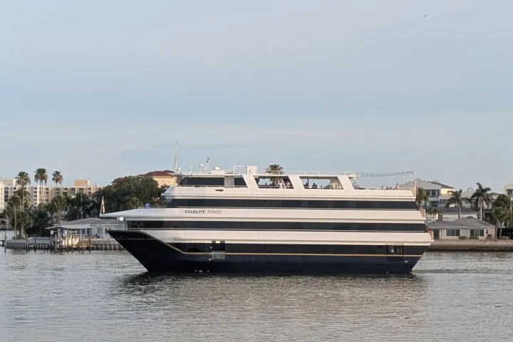 Large yacht sailing near a coastal city with palm trees.
