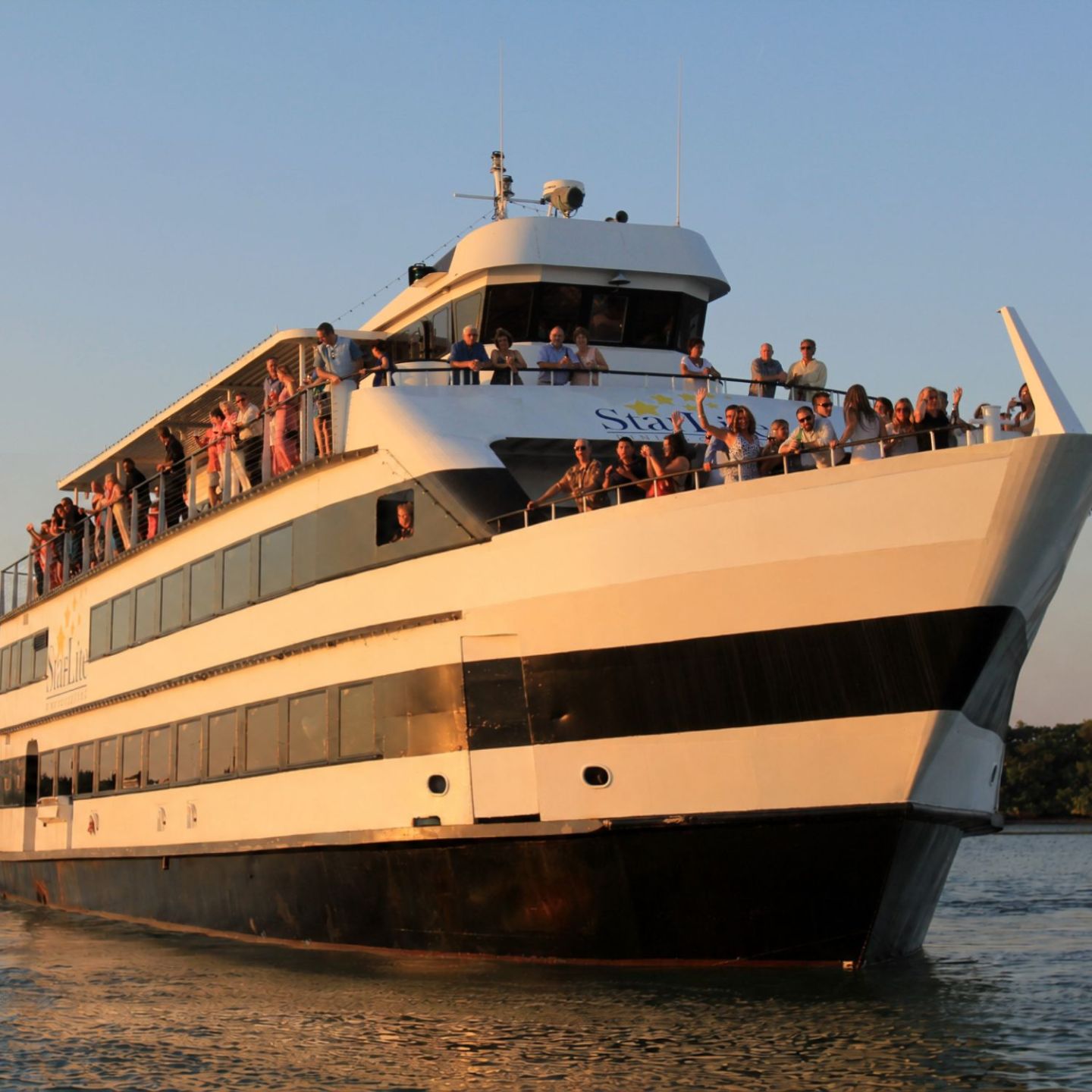 Large cruise ship with people on deck against a clear sky.