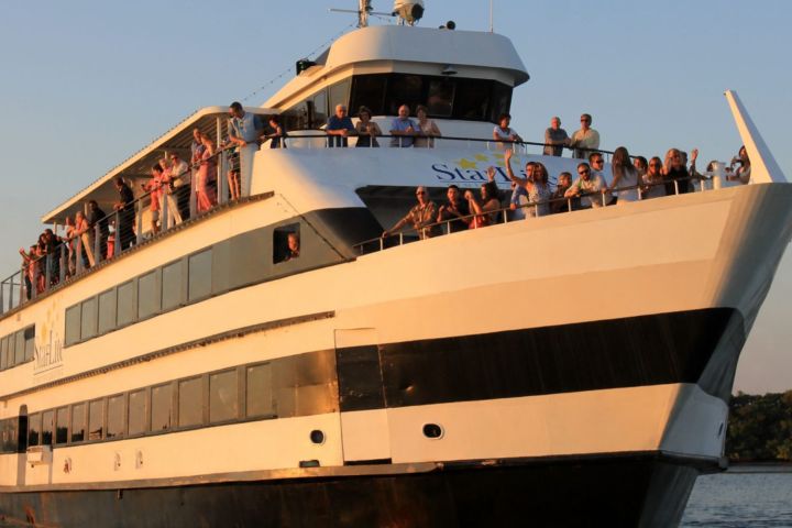 Large cruise ship with people on deck against a clear sky.
