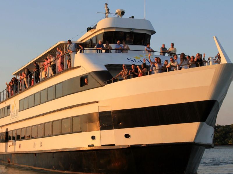 Large cruise ship with people on deck against a clear sky.