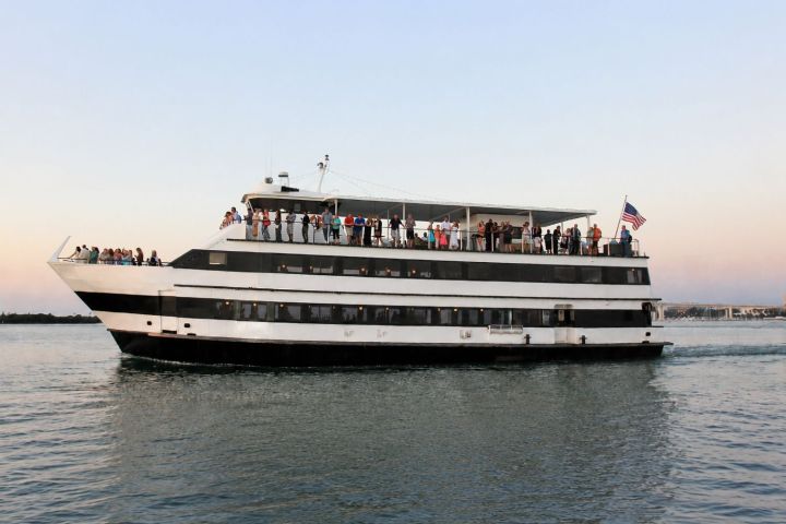 Large, three-deck yacht with passengers on water, American flag flying.