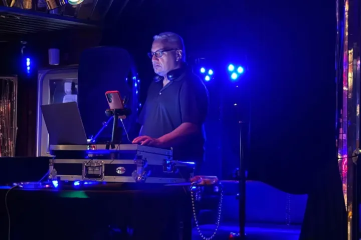 DJ performing with equipment and laptop in a dimly lit venue