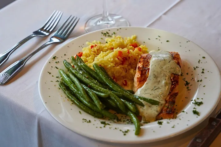 Plate with grilled salmon, green beans, rice, and a glass of white wine on a table.