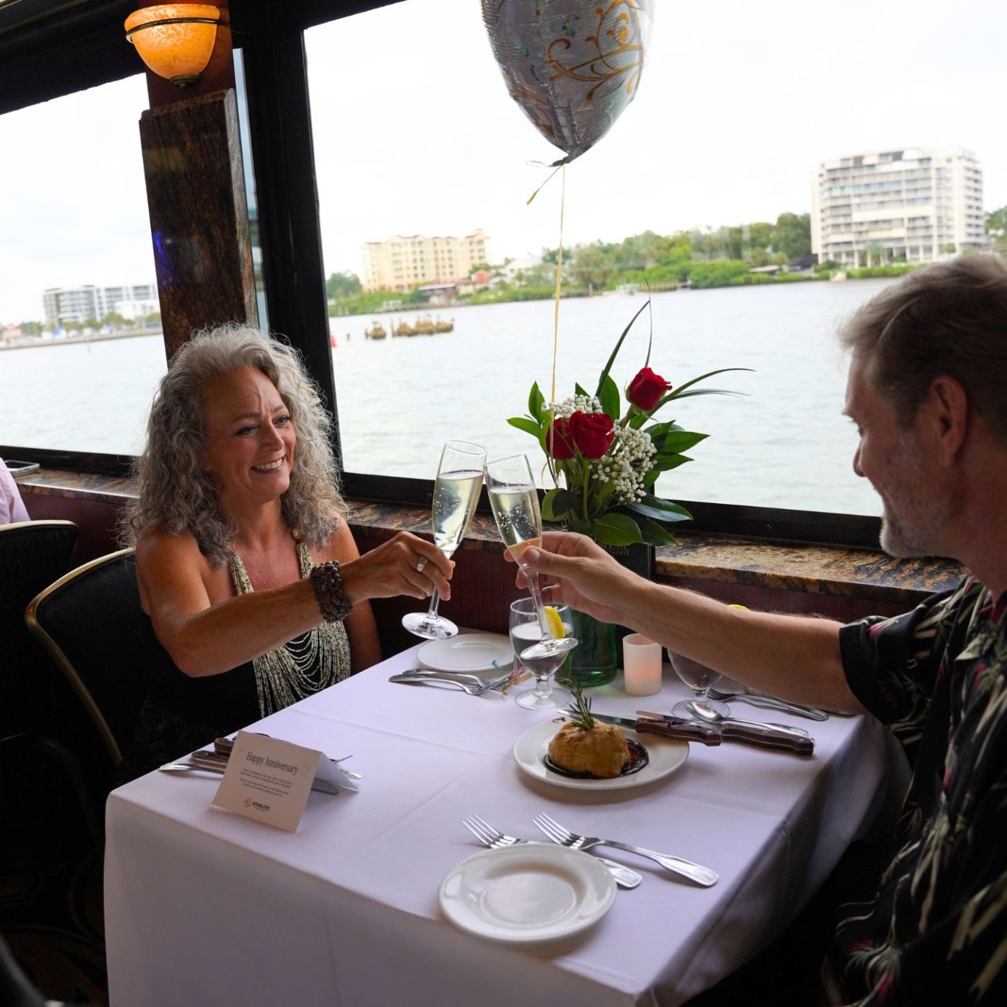 Couple toasting at a restaurant with a river view.