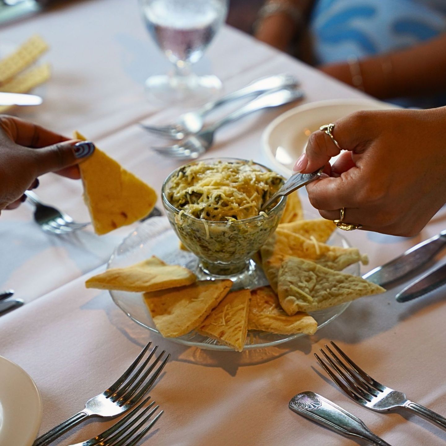 Two hands dipping chips into spinach artichoke dip on a table.