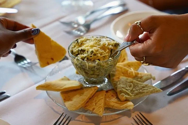 Two hands dipping chips into spinach artichoke dip on a table.