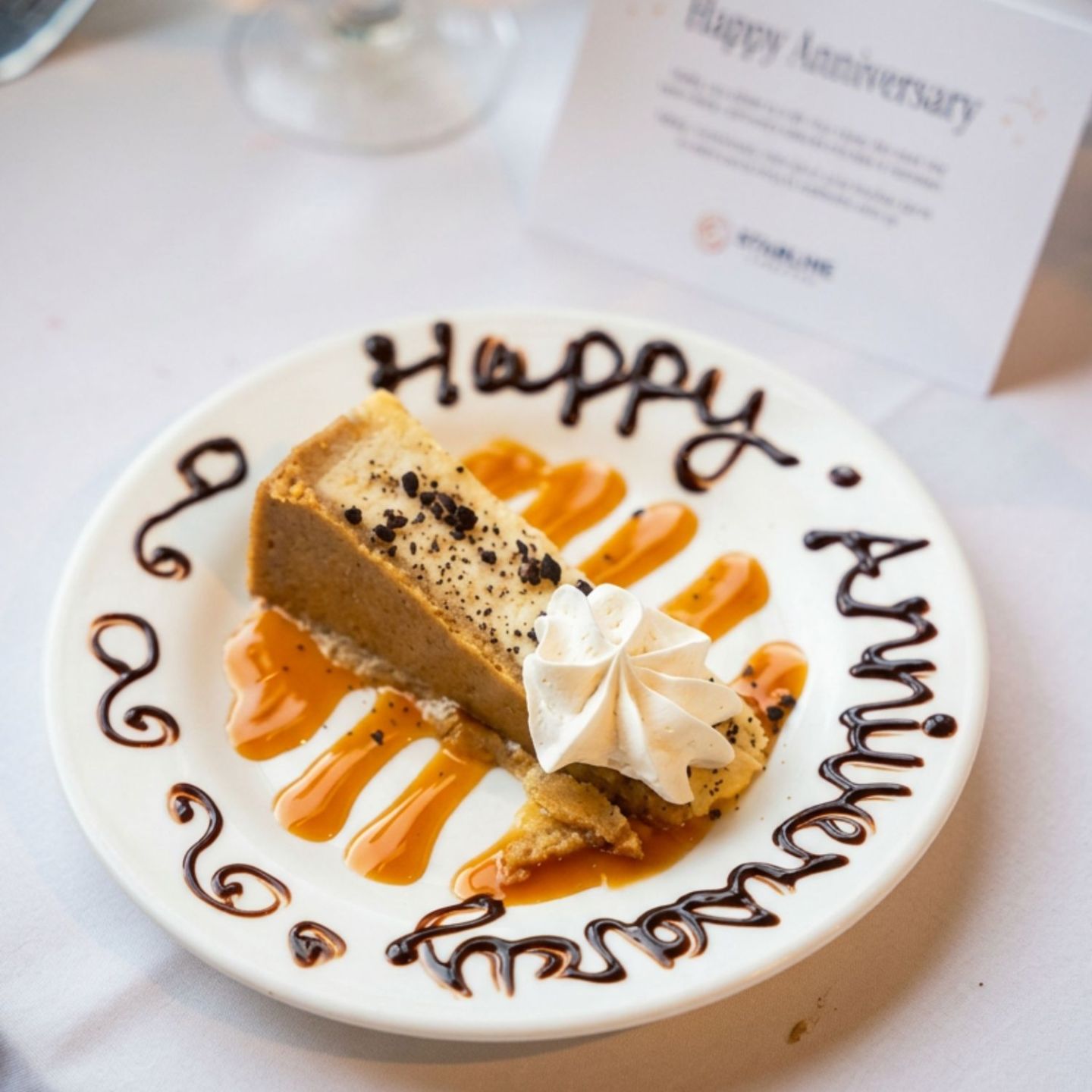 Cheesecake slice with whipped cream on a decorated 'Happy Anniversary' plate.