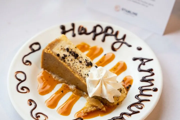 Cheesecake slice with whipped cream on a decorated 'Happy Anniversary' plate.
