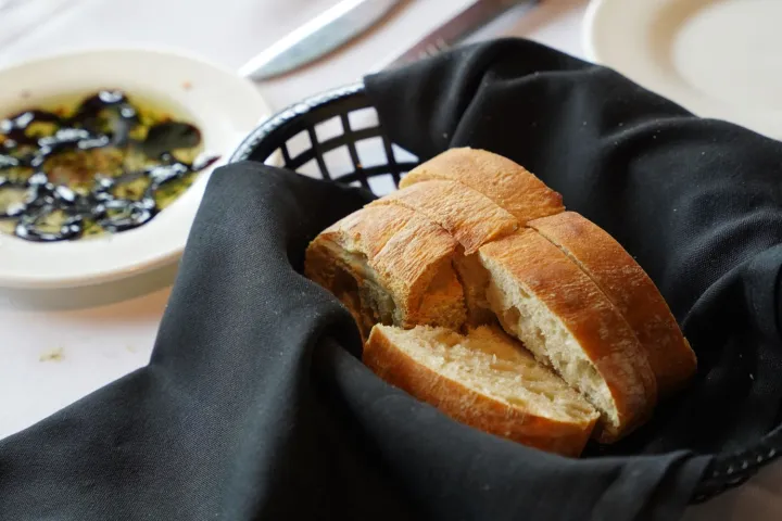 Basket with sliced bread on black cloth, dipping oil on side.