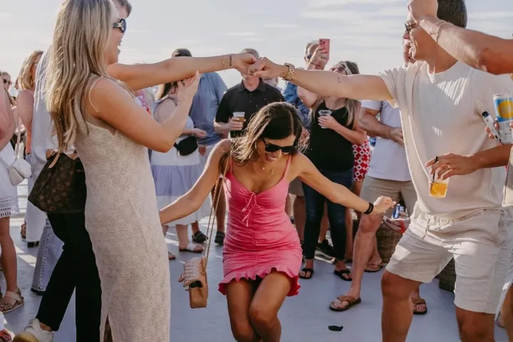 Group of people dancing outdoors at a party with string lights overhead.