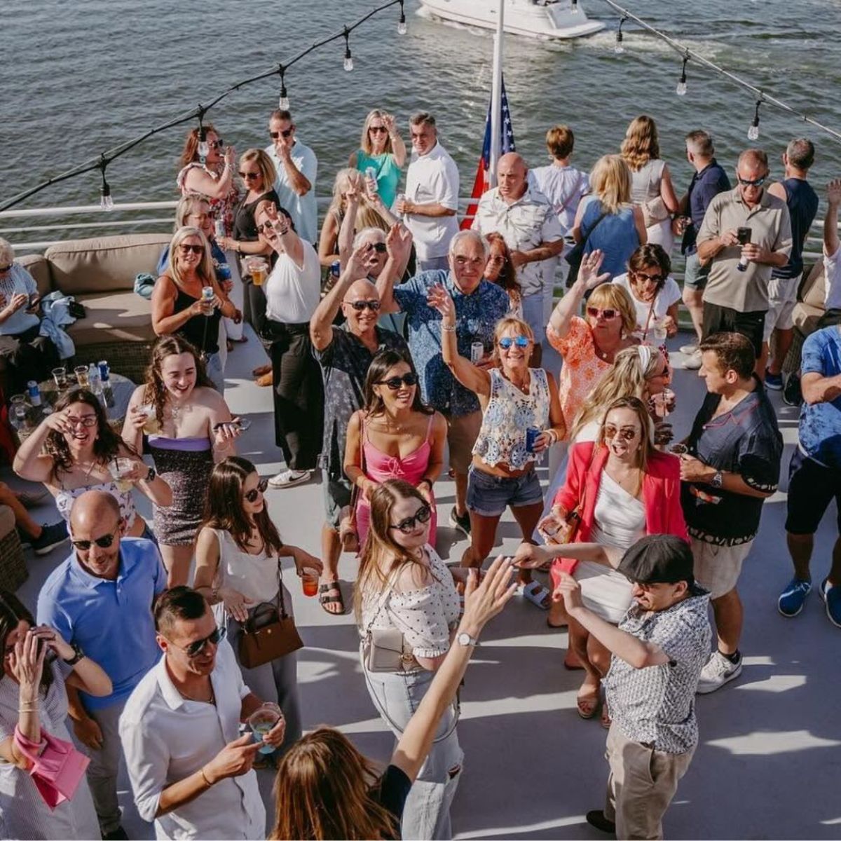 Group of people celebrating on a boat with decorations and water in the background.