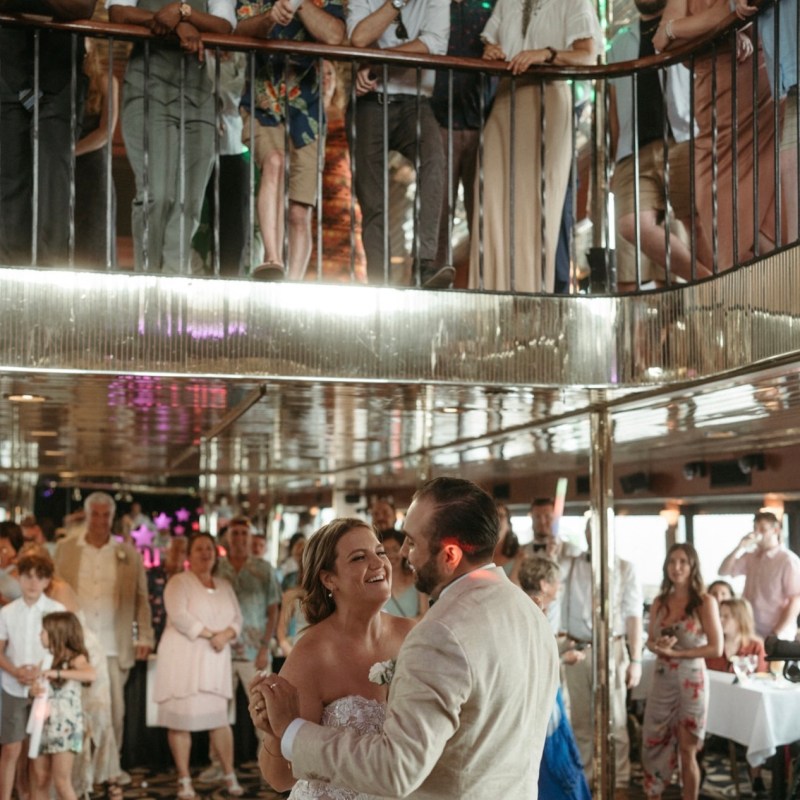 Couple dancing at wedding reception, guests watching from upper level.