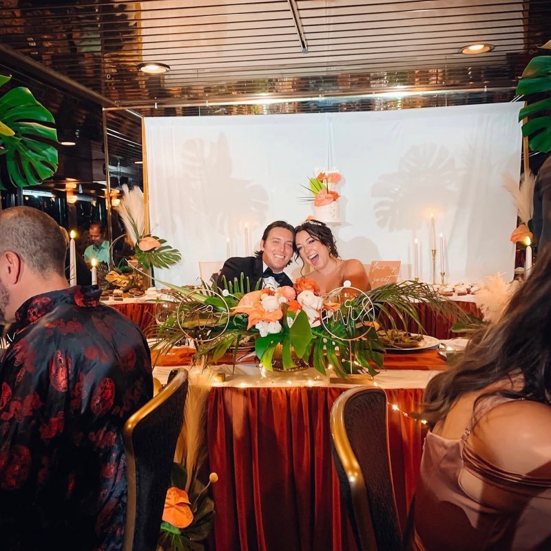 Couple smiling at decorated wedding table with floral arrangements and candles.