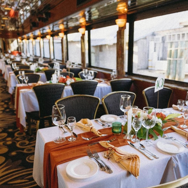 Elegant dining tables in a train car with white tablecloths and floral decor.