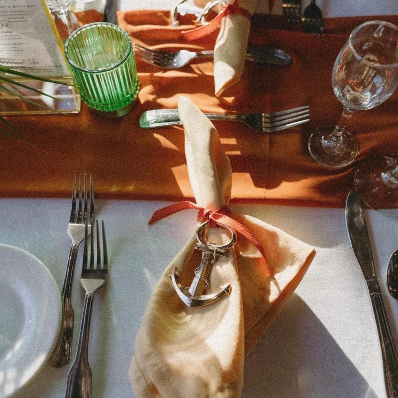 Table setting with napkin tied with anchor charm on a brown runner.