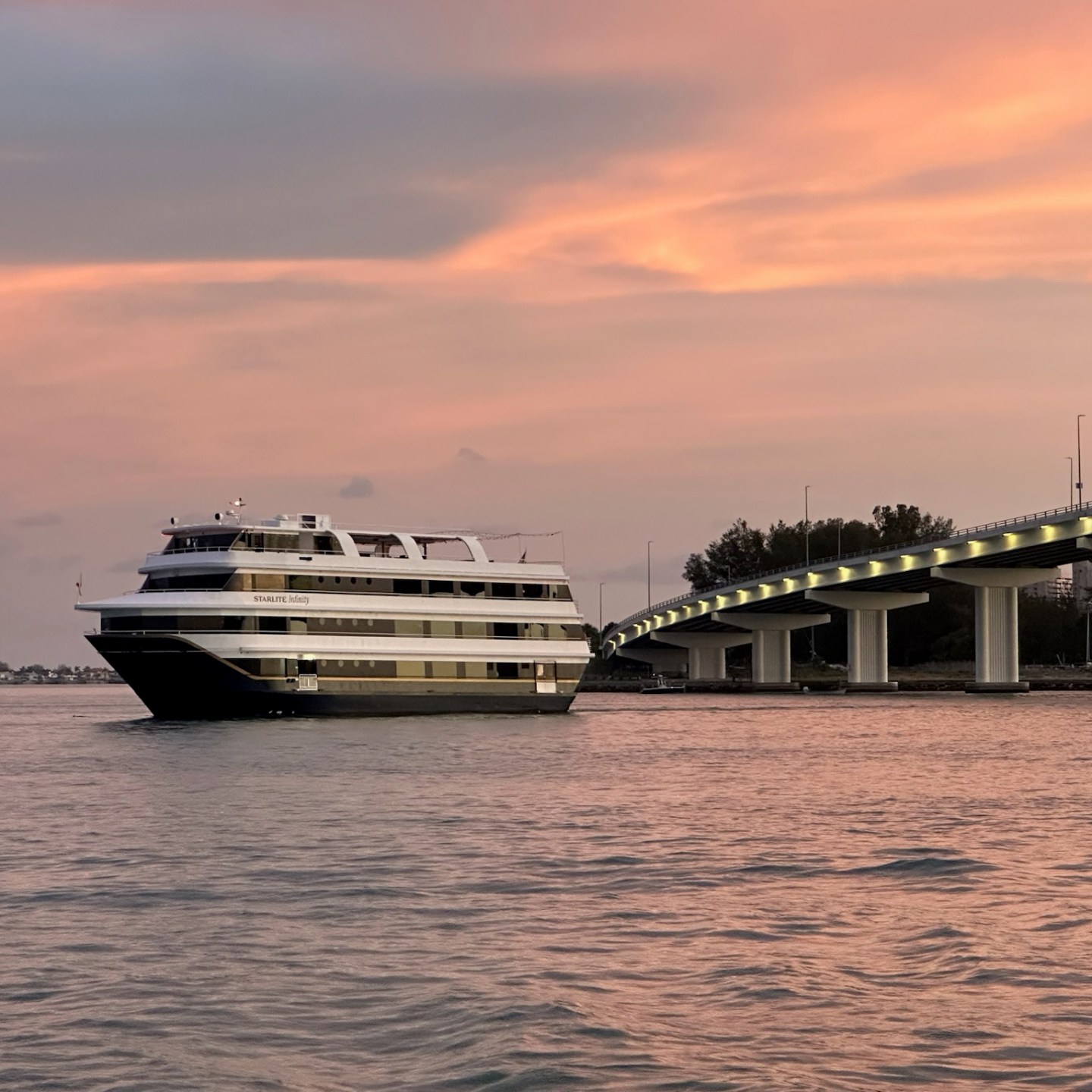 Large boat near bridge at sunset over calm water.