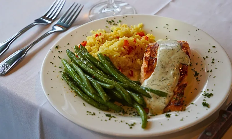 Grilled salmon with sauce, green beans, and rice on a white plate.