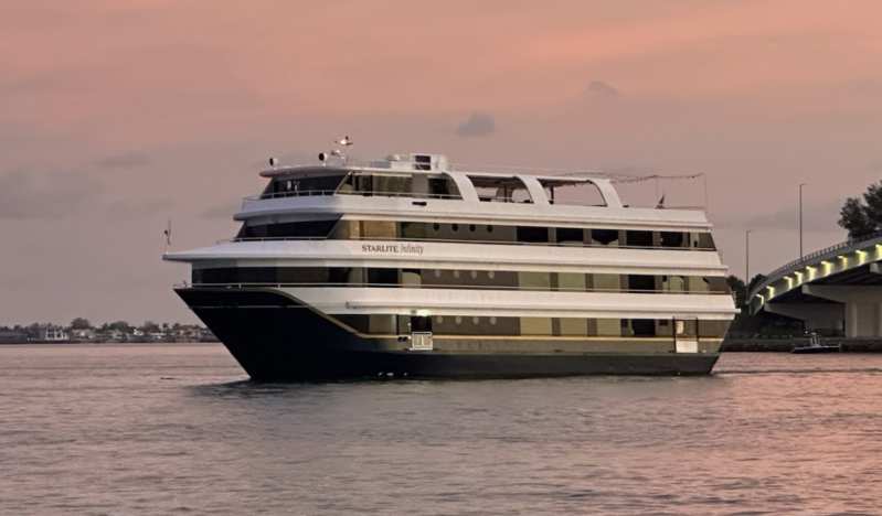 A large white and black cruise ship near a bridge at sunset.