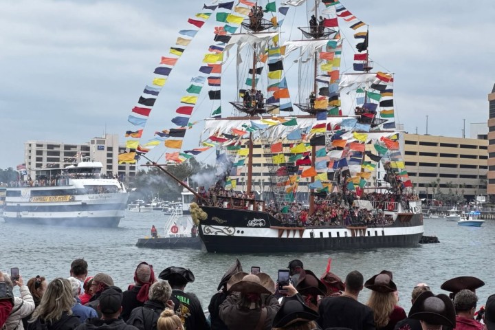 Colorful pirate ship with flags sails in harbor during festival.