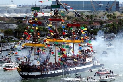 Colorful pirate ship with flags in a crowded marina parade.