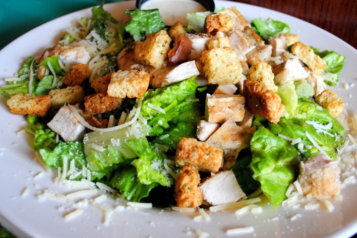 Plate of chicken Caesar salad with croutons and parmesan cheese.