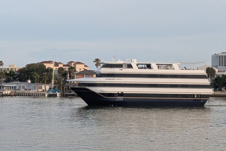 Large yacht sailing near waterfront homes and palm trees.