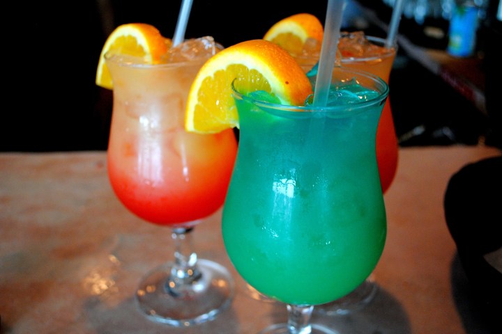 Three colorful cocktails with orange slices on a bar.