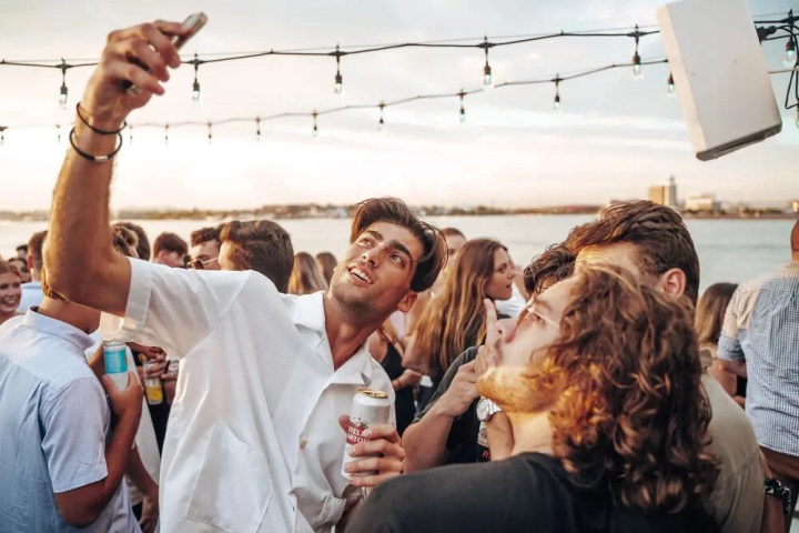 Group of friends taking a selfie at an outdoor party by the water.